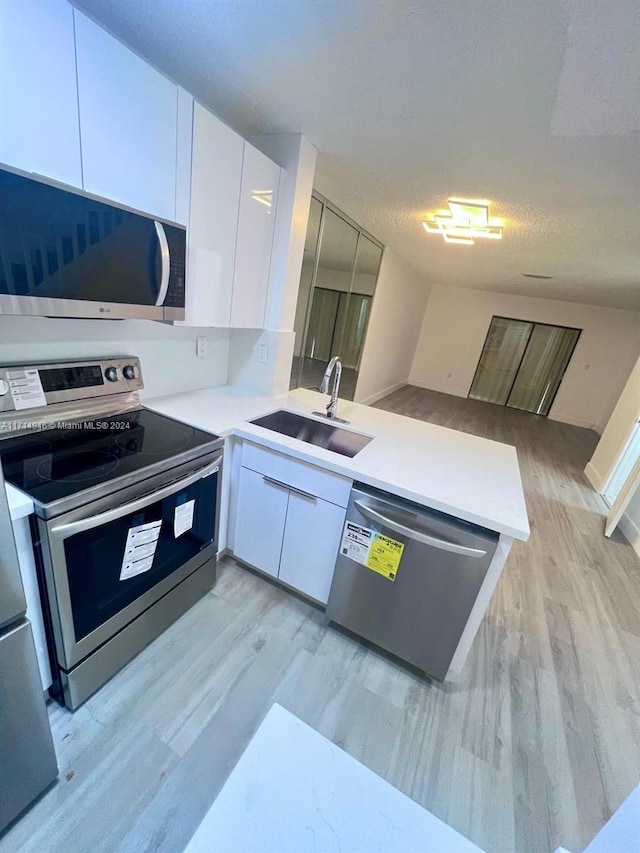 kitchen featuring kitchen peninsula, appliances with stainless steel finishes, a textured ceiling, sink, and white cabinets