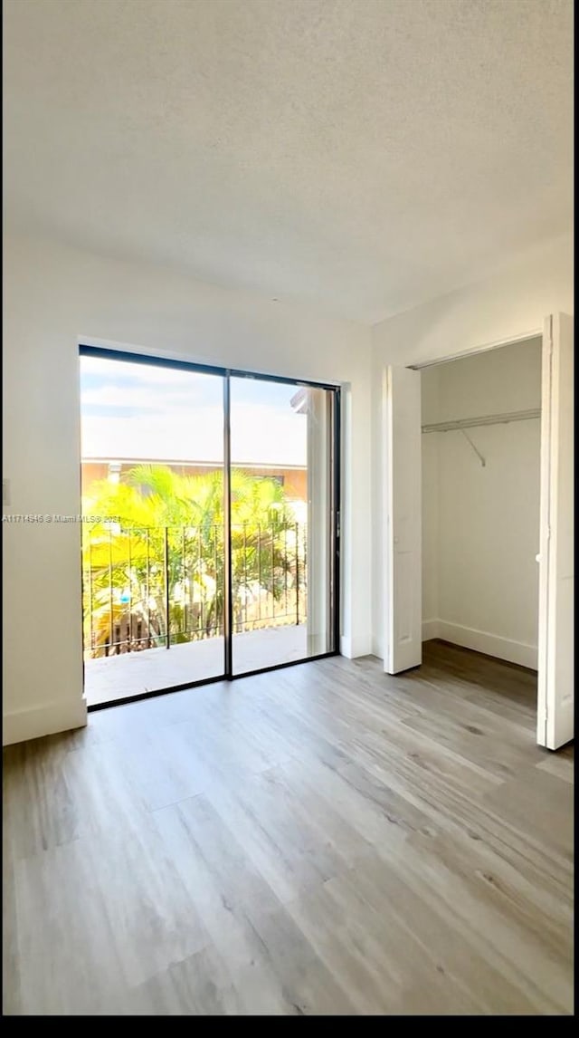 unfurnished bedroom with access to exterior, a textured ceiling, light hardwood / wood-style floors, and a closet