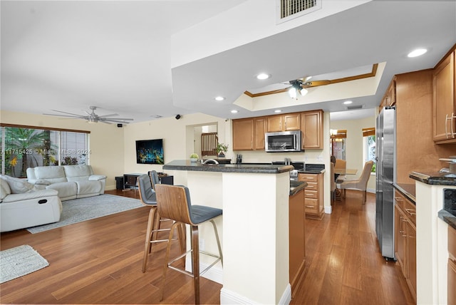 kitchen featuring a kitchen breakfast bar, hardwood / wood-style flooring, ceiling fan, a tray ceiling, and stainless steel appliances