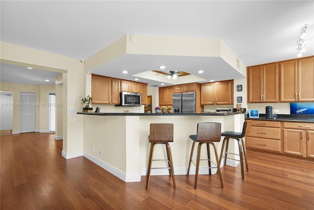 kitchen with dark hardwood / wood-style floors, ceiling fan, appliances with stainless steel finishes, kitchen peninsula, and a breakfast bar area