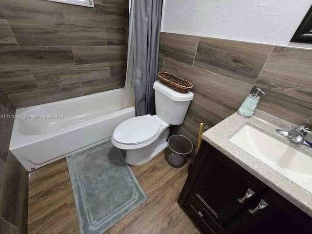 full bathroom featuring vanity, shower / tub combo with curtain, hardwood / wood-style flooring, tile walls, and toilet