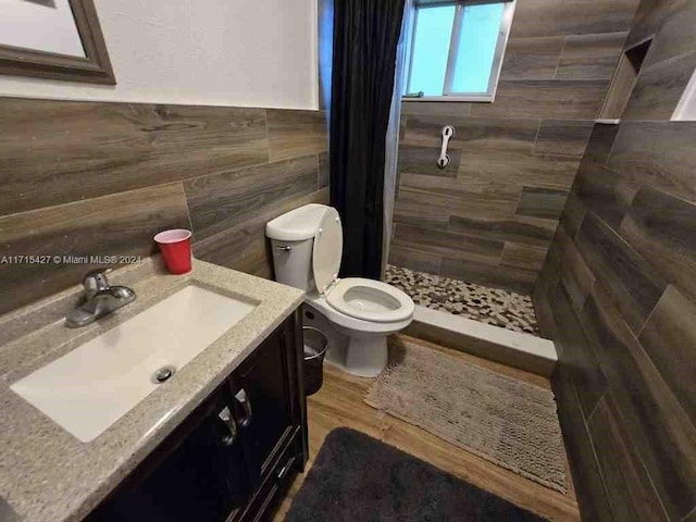 bathroom with hardwood / wood-style floors, toilet, tiled shower, vanity, and tile walls