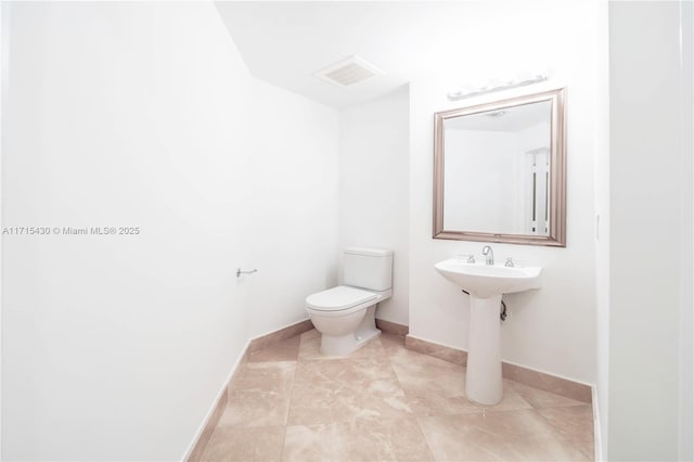 half bathroom with toilet, a sink, visible vents, baseboards, and tile patterned floors