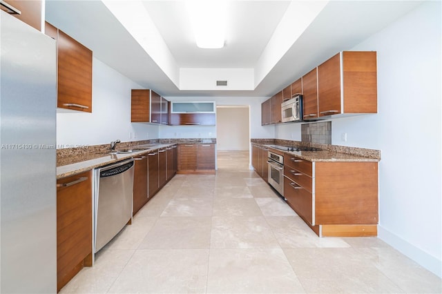 kitchen featuring appliances with stainless steel finishes, light stone countertops, open shelves, a tray ceiling, and brown cabinetry