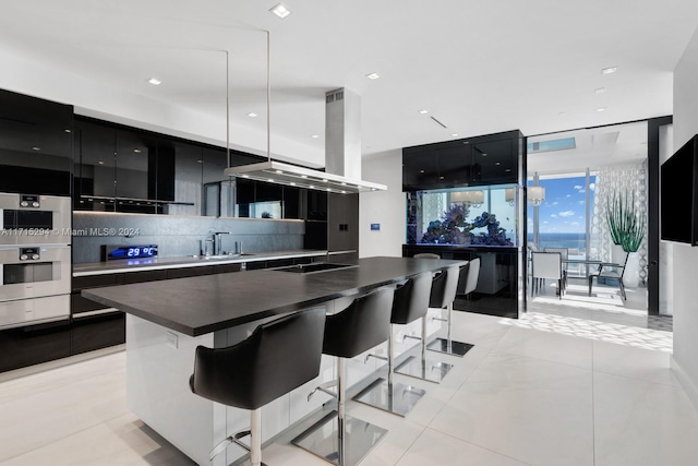 kitchen with light tile patterned flooring, decorative light fixtures, a breakfast bar area, island range hood, and a kitchen island