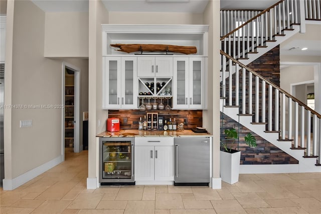 bar with decorative backsplash, beverage cooler, stainless steel refrigerator, and white cabinets