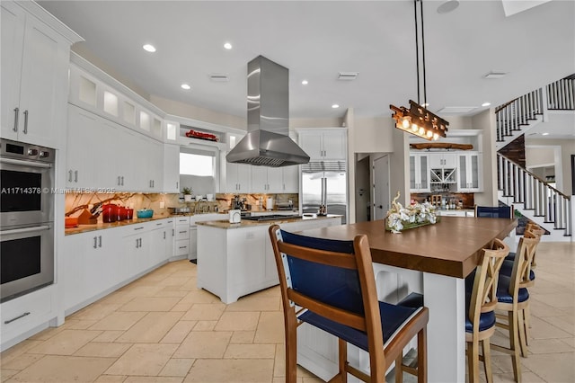 kitchen featuring pendant lighting, appliances with stainless steel finishes, white cabinetry, island range hood, and a kitchen island