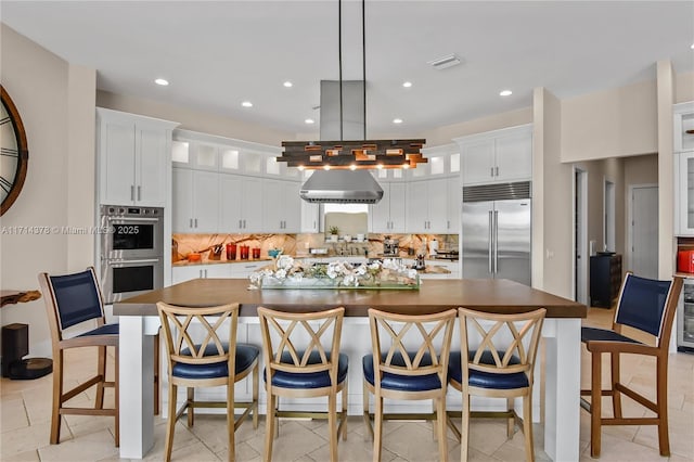 kitchen featuring a kitchen bar, decorative light fixtures, a center island with sink, stainless steel appliances, and white cabinets