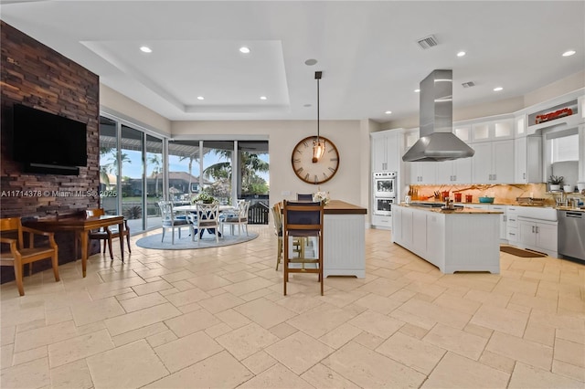 kitchen with pendant lighting, white cabinetry, island range hood, a center island with sink, and decorative backsplash