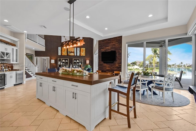 kitchen with white cabinets, a kitchen breakfast bar, hanging light fixtures, a center island, and a raised ceiling