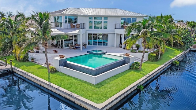 back of house with a swimming pool with hot tub, a yard, a patio, a water view, and a balcony