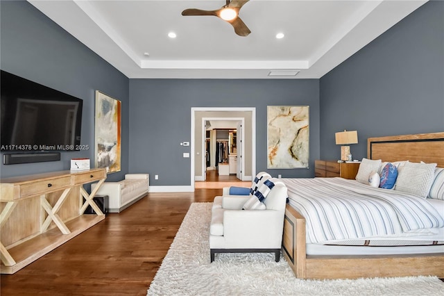 bedroom with ceiling fan, a tray ceiling, dark hardwood / wood-style floors, and a spacious closet