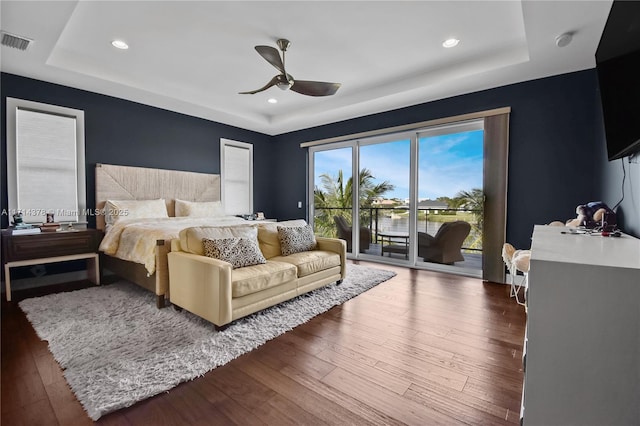 bedroom with a raised ceiling, dark hardwood / wood-style floors, access to exterior, and ceiling fan