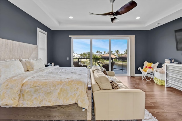 bedroom with ceiling fan, access to outside, dark hardwood / wood-style flooring, and a tray ceiling