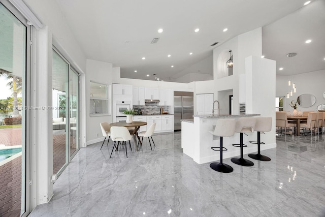 kitchen featuring white cabinetry, built in fridge, light stone counters, kitchen peninsula, and a breakfast bar area