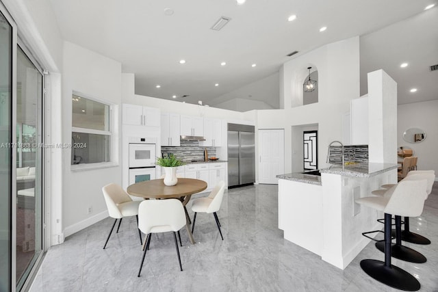 kitchen with light stone counters, double oven, kitchen peninsula, built in refrigerator, and decorative backsplash