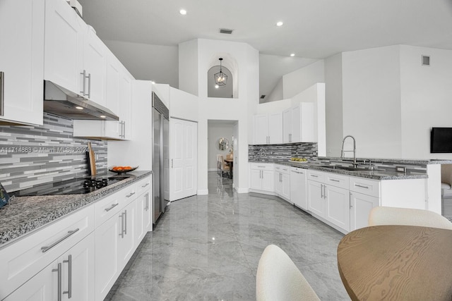 kitchen with dark stone countertops, built in fridge, sink, and white cabinets