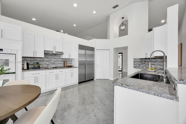 kitchen with tasteful backsplash, light stone counters, sink, stainless steel built in fridge, and white cabinetry