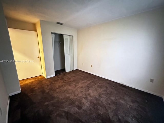 unfurnished bedroom with dark carpet and a closet