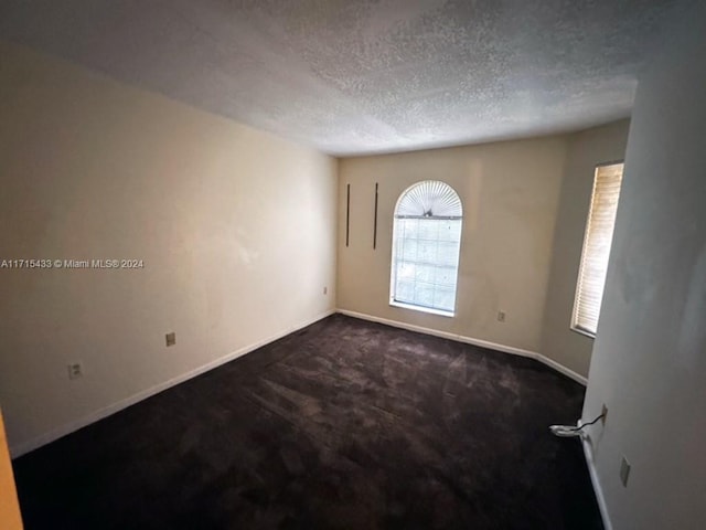 empty room with dark carpet and a textured ceiling