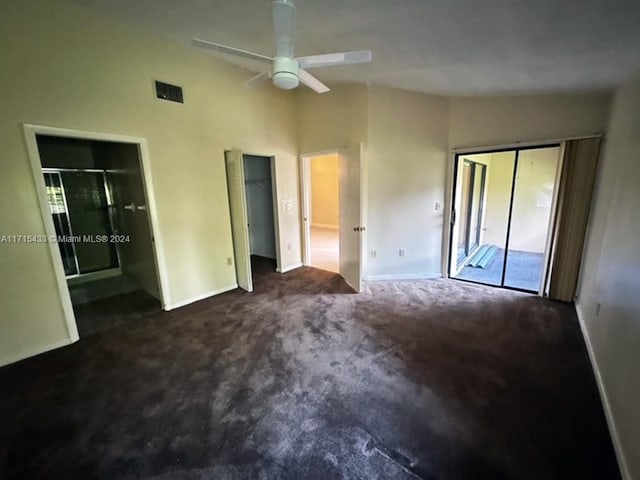 unfurnished bedroom featuring dark colored carpet, vaulted ceiling, ceiling fan, and multiple closets