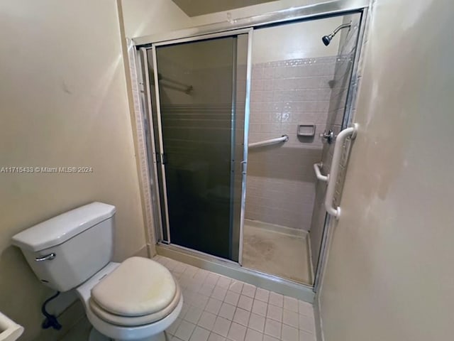 bathroom with tile patterned flooring, toilet, and a shower with door