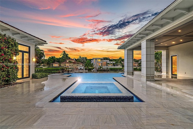 pool at dusk with a patio area and an in ground hot tub