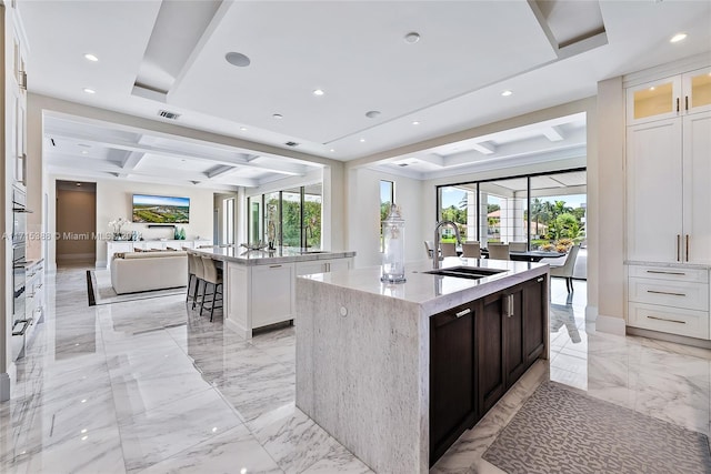 kitchen featuring a kitchen breakfast bar, sink, white cabinetry, and a kitchen island with sink