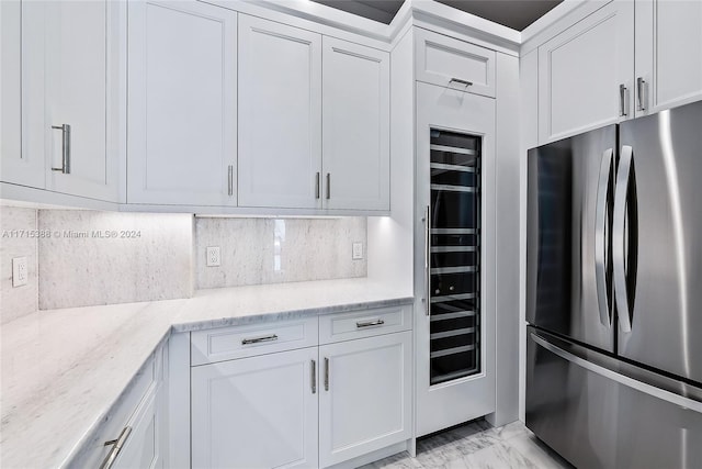 kitchen with white cabinets, light stone countertops, backsplash, and stainless steel refrigerator