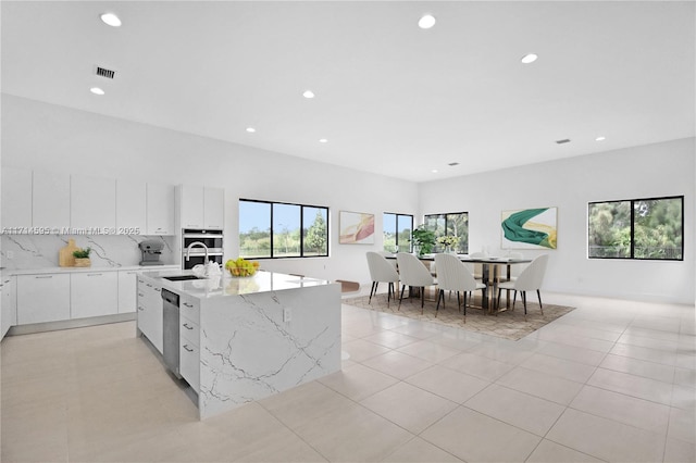 kitchen with appliances with stainless steel finishes, tasteful backsplash, white cabinets, a kitchen island with sink, and light tile patterned floors