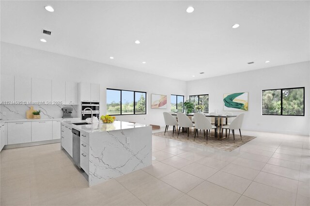 kitchen with a wealth of natural light, white cabinets, an island with sink, and stainless steel appliances