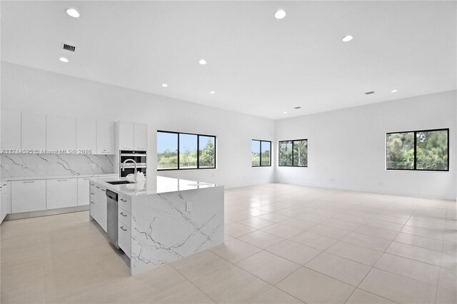 kitchen with stainless steel appliances, light tile patterned floors, white cabinets, and a spacious island