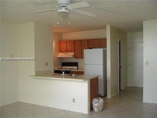 kitchen featuring kitchen peninsula, ceiling fan, light tile patterned floors, and white appliances