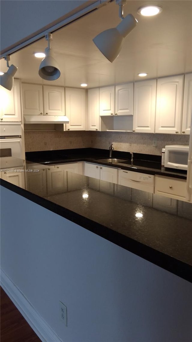 kitchen featuring white appliances, sink, decorative light fixtures, dark stone countertops, and white cabinetry