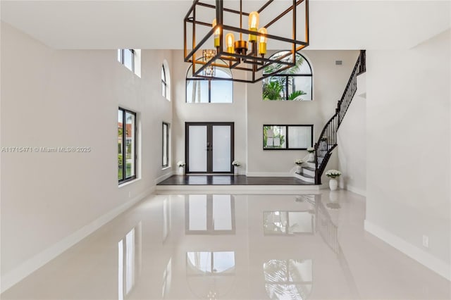 entrance foyer with an inviting chandelier, a towering ceiling, and french doors