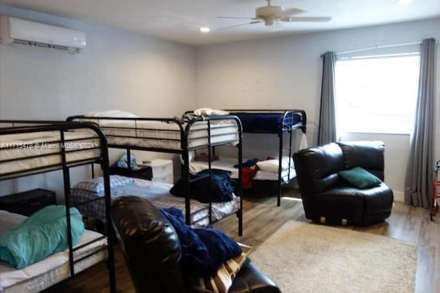 bedroom with a wall mounted AC, ceiling fan, and wood-type flooring