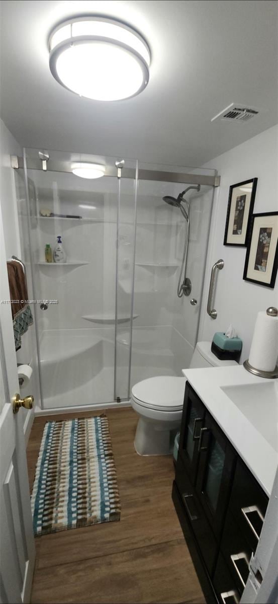 bathroom featuring a stall shower, visible vents, toilet, wood finished floors, and vanity