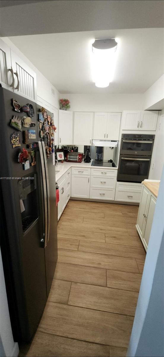 kitchen featuring under cabinet range hood, white cabinetry, light countertops, light wood-type flooring, and black appliances