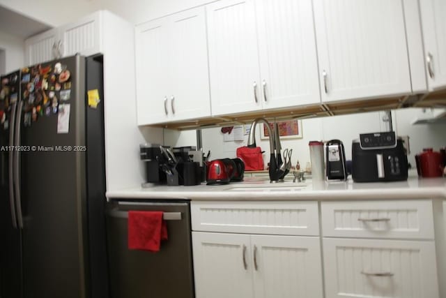 kitchen featuring light countertops, stainless steel dishwasher, freestanding refrigerator, and white cabinetry