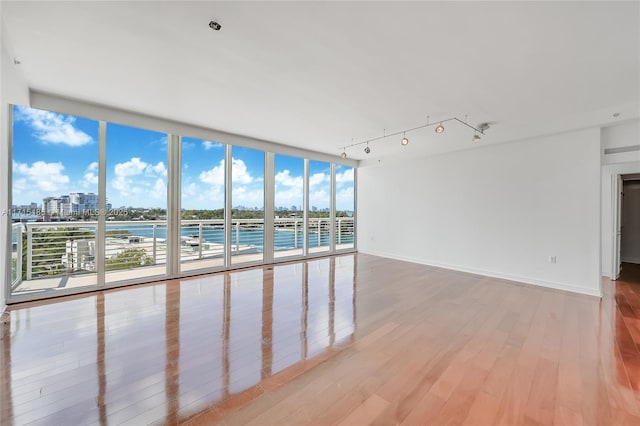 empty room featuring light wood finished floors, baseboards, floor to ceiling windows, track lighting, and a view of city