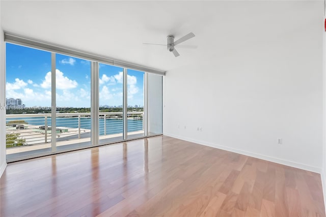 spare room featuring expansive windows, wood finished floors, a ceiling fan, and baseboards