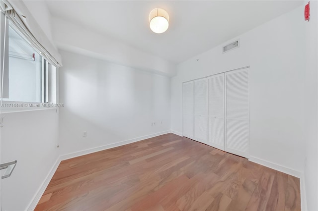 unfurnished bedroom featuring a closet, wood finished floors, visible vents, and baseboards