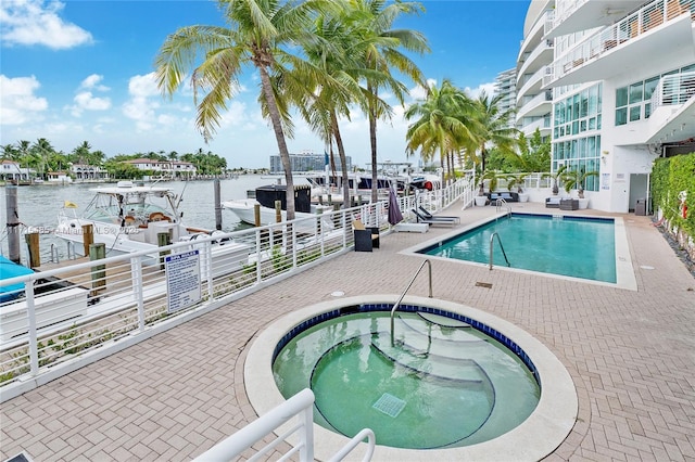 pool with a patio area, a hot tub, and a water view