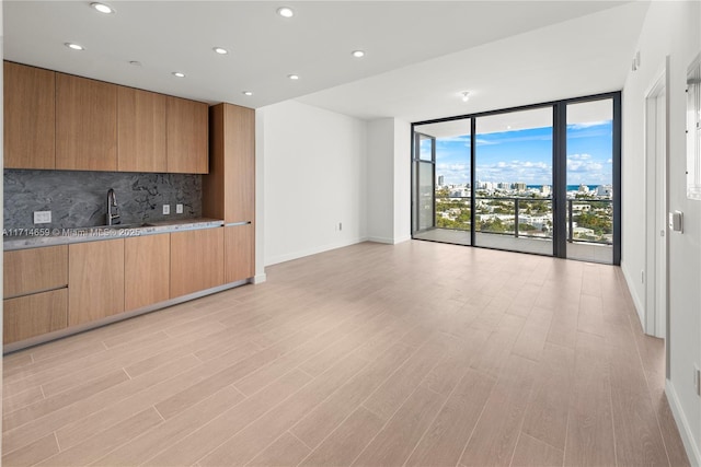 interior space with sink, light hardwood / wood-style flooring, floor to ceiling windows, light stone countertops, and decorative backsplash