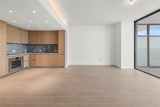 kitchen with sink, light wood-type flooring, expansive windows, oven, and backsplash