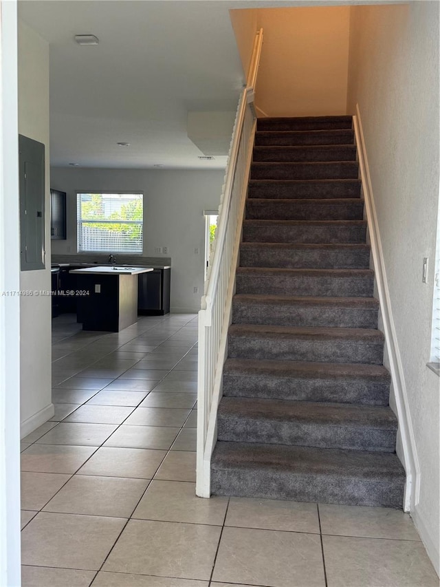 stairway featuring tile patterned floors, electric panel, and sink