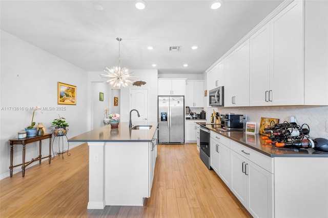 kitchen featuring an island with sink, sink, white cabinets, hanging light fixtures, and stainless steel appliances