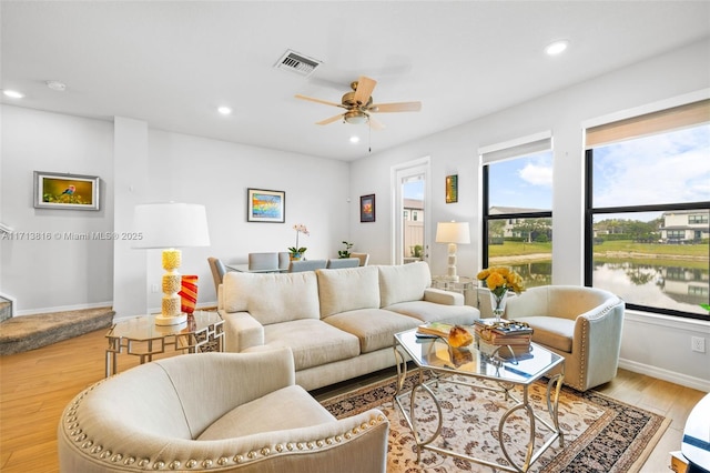 living room with light wood-type flooring, ceiling fan, and a water view