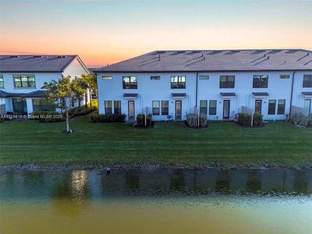 back of house at dusk featuring a yard, stucco siding, and a water view