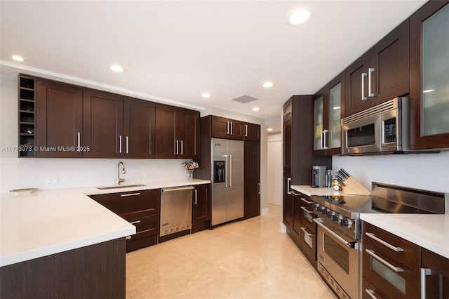 kitchen featuring high end appliances, sink, light tile patterned floors, and dark brown cabinets